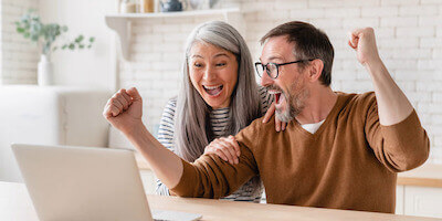 The main benefits of selling your house at auction - couple celebrate selling their house by auction in front of a laptop