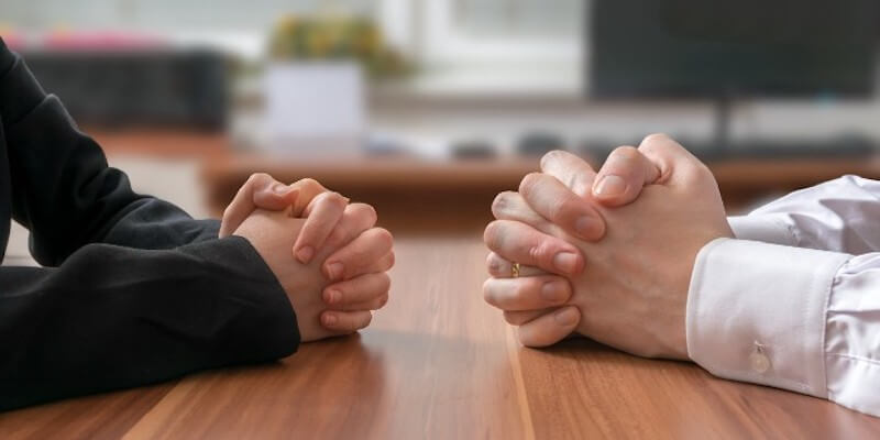 Image of two people in negotiations sat opposite each other with hands clasped: Pre-auction sales involve negotiations.