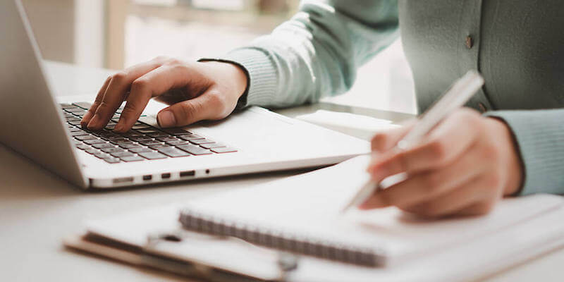 Image of a lady researching on a laptop and making notes. What do you need to do before bidding at an auction?