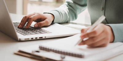 Image of a lady researching on a laptop and making notes. What do you need to do before bidding at an auction?
