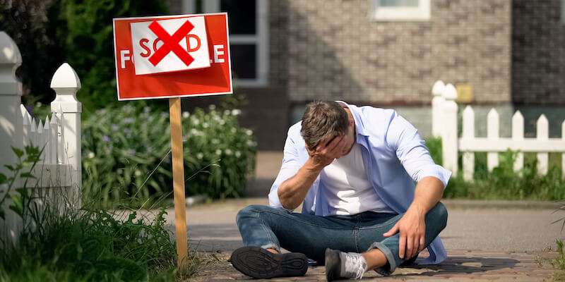 Man sitting on the ground in front of his house after house sale fallen through