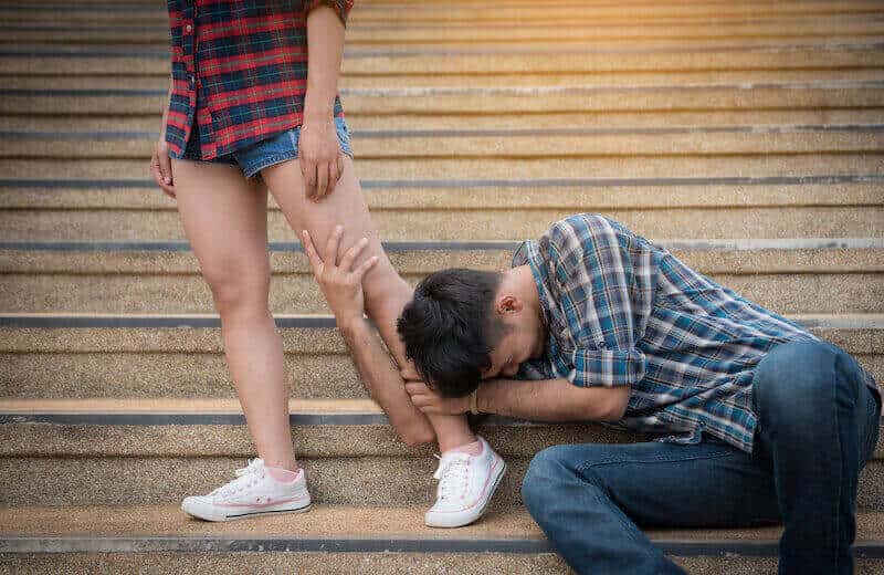 A woman walks away from a man holding her leg.