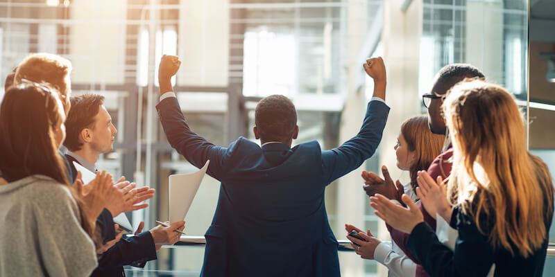 Image of a man celebrating, and being cheered by his co-workers. Presumably after breaking the housing chain. 