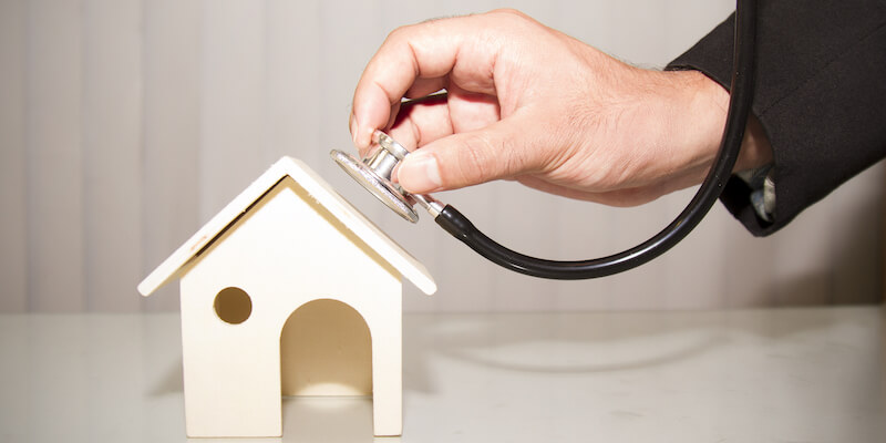Man using stethoscope with house to diagnose subsidence problem. How to fix subsidence. 