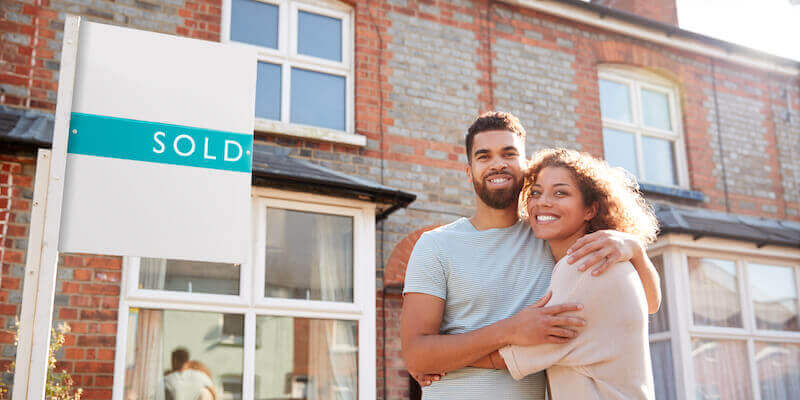 A happy couple standing outside a property that they've just sold. 7 ways to improve your chances of selling a BISF house. 
