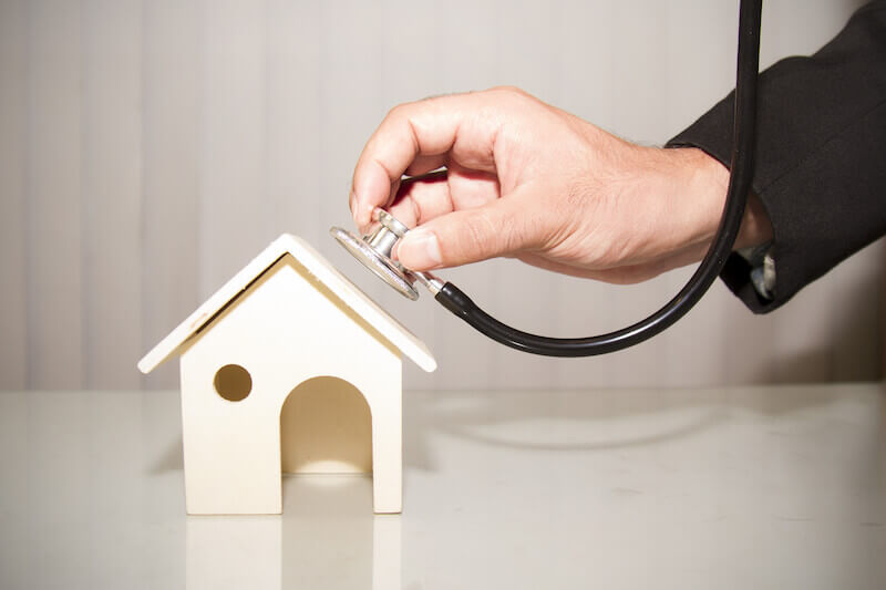 An image of a man using a stethoscope on a toy house.