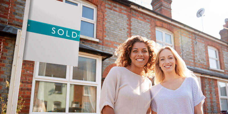 Image of two women standing outside home with sold sign. What's the best way to sell a wimpey no-fines house? My 5 top tips. 