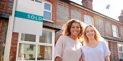 Image of two women standing outside home with sold sign. What's the best way to sell a wimpey no-fines house? My 5 top tips. 