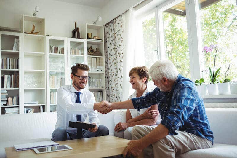 A couple shaking hands with an estate agent in their home.