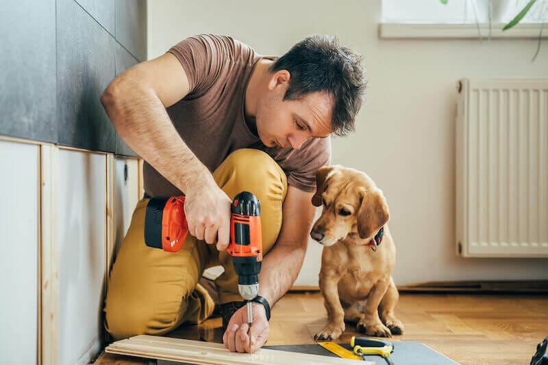 A man carrying out DIY repairs to his home with a pet dog sat next to him.