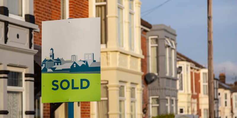 An estate agents sold sign outside a row of houses. How to sell your house fast for the best price: my 9 top tips. 