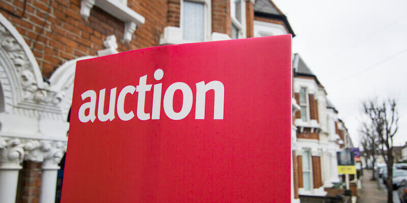 An auction for sale sign on a street of terraced houses. Traditional auction versus modern method of auction.