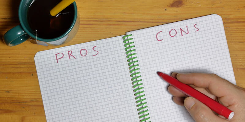 Pros and cons list in a notebook with a man writing in red marker. Modern Auction: The Top 15 Pros & Cons.